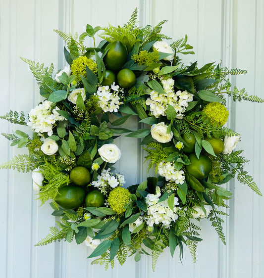 Green and white botanical wreath with faux limes and mixed greenery on neutral siding background.