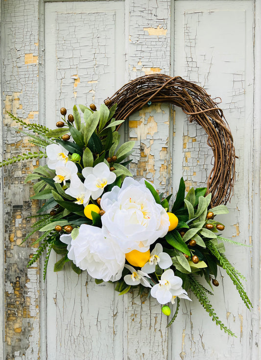 White peony and citrus elements define the Martini floral wreath, layered with fresh greenery and shown against a vintage door