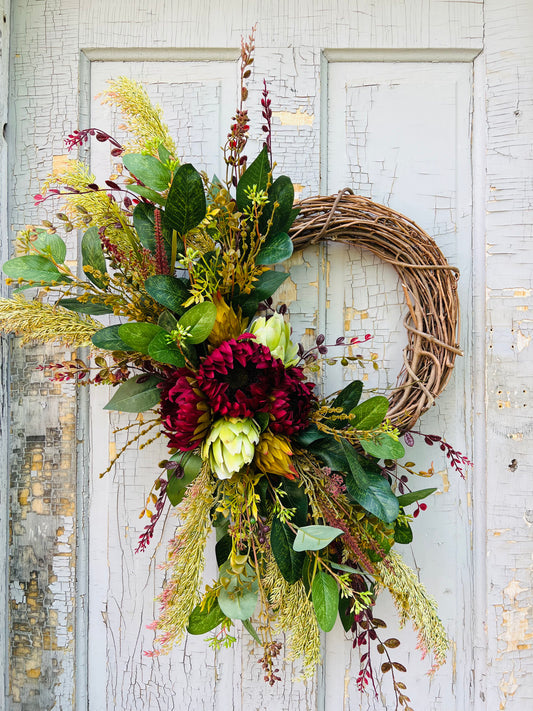 Autumn’s Garden botanical wreath design featuring sunflower blooms, artichoke accents, and seasonal greenery styled on a vintage paneled door