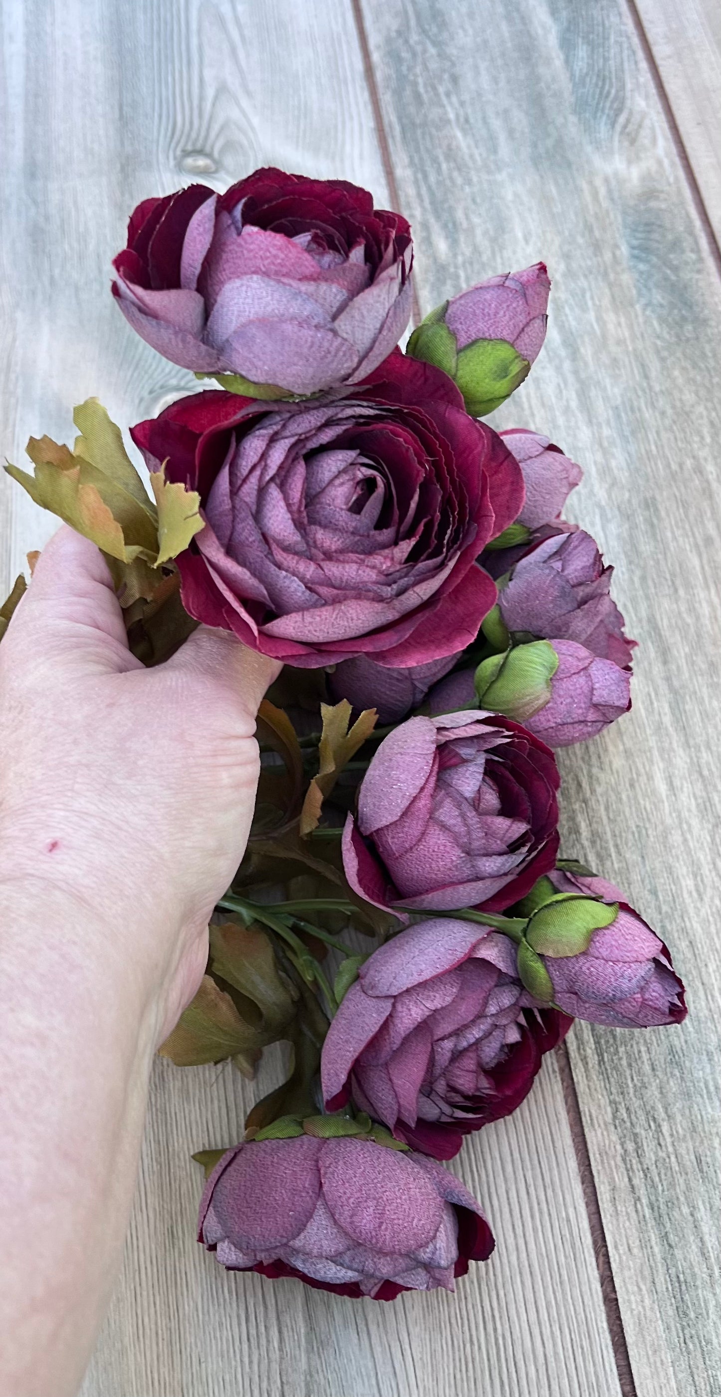 A hand holding a bloom from the artificial ranunculus bundle showcasing layered petals, realistic buds, and natural scale.