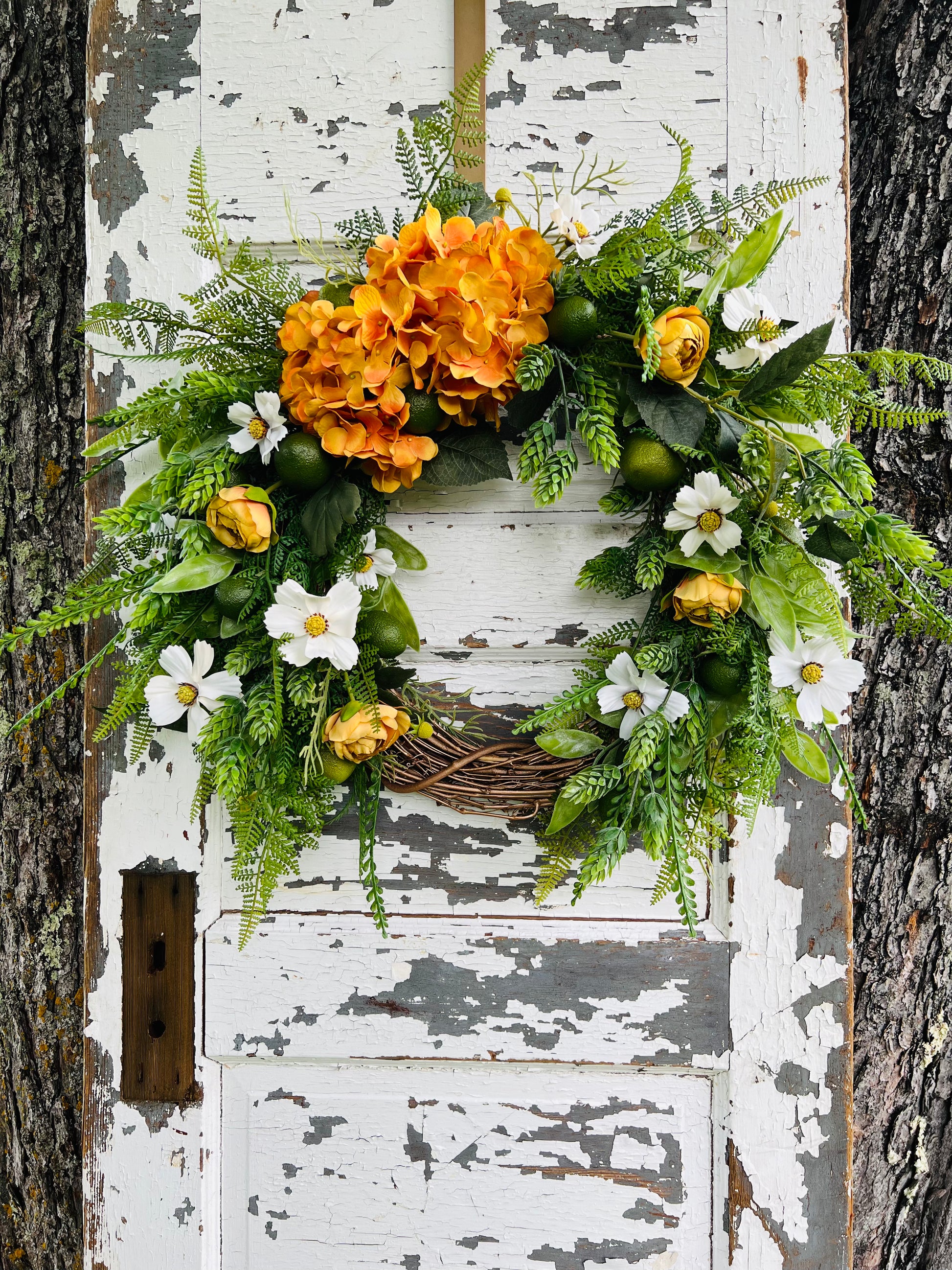 Gardenbug Designs Moscow Mule botanical wreath featuring copper hydrangeas, ranunculus, citrus accents, and layered greenery styled on a rustic garden door