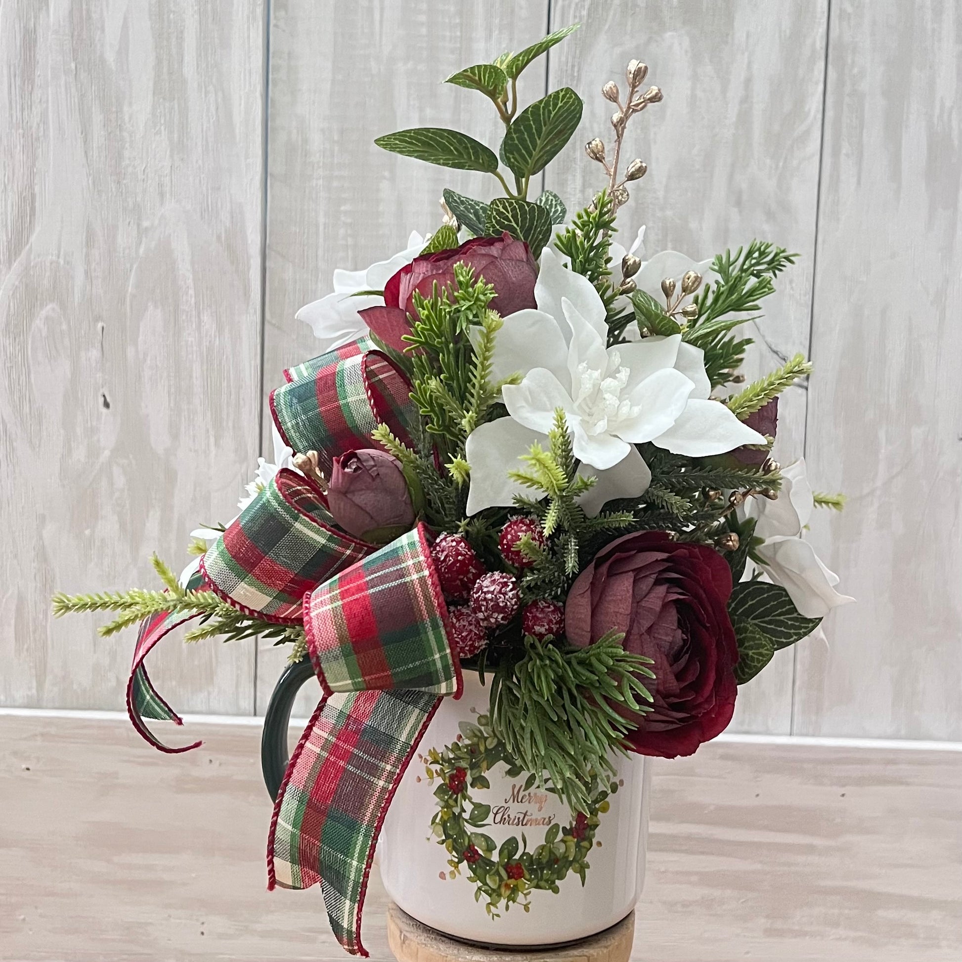 Burgundy ranunculus stems styled in a holiday coffee mug arrangement with greenery and ribbon, illustrating scale, color pairing, and design potential