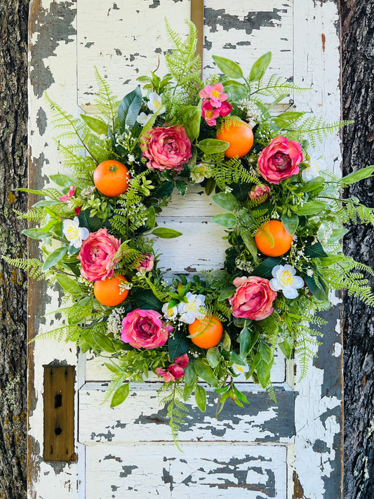Valencia Gardens citrus floral wreath with  oranges, ranunculus, cosmos, and lush greenery on a rustic white door by Gardenbug Designs.