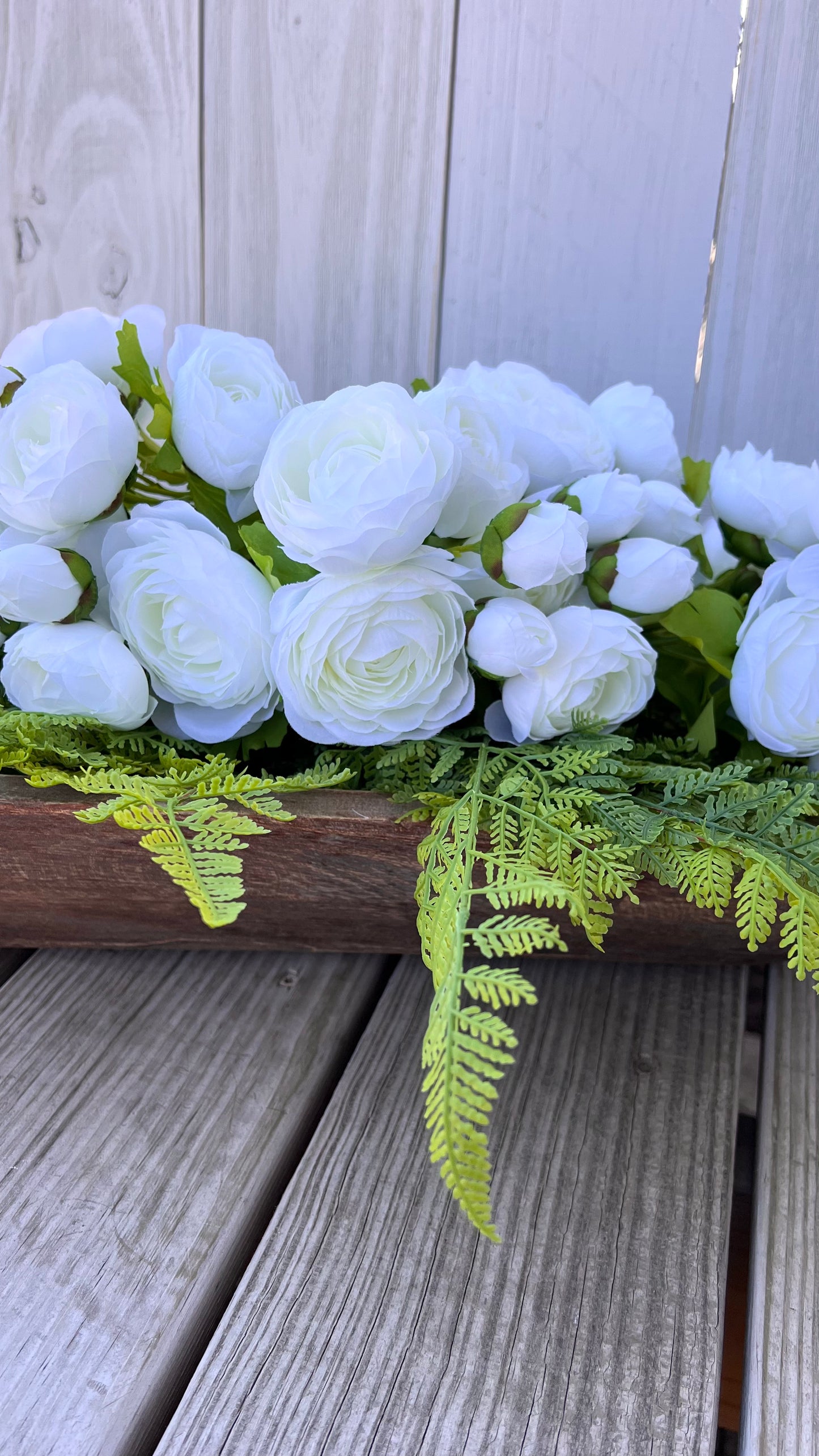 White ranunculus bundle styled in a wooden dough bowl with fern greenery, showing natural movement and depth in a layered composition