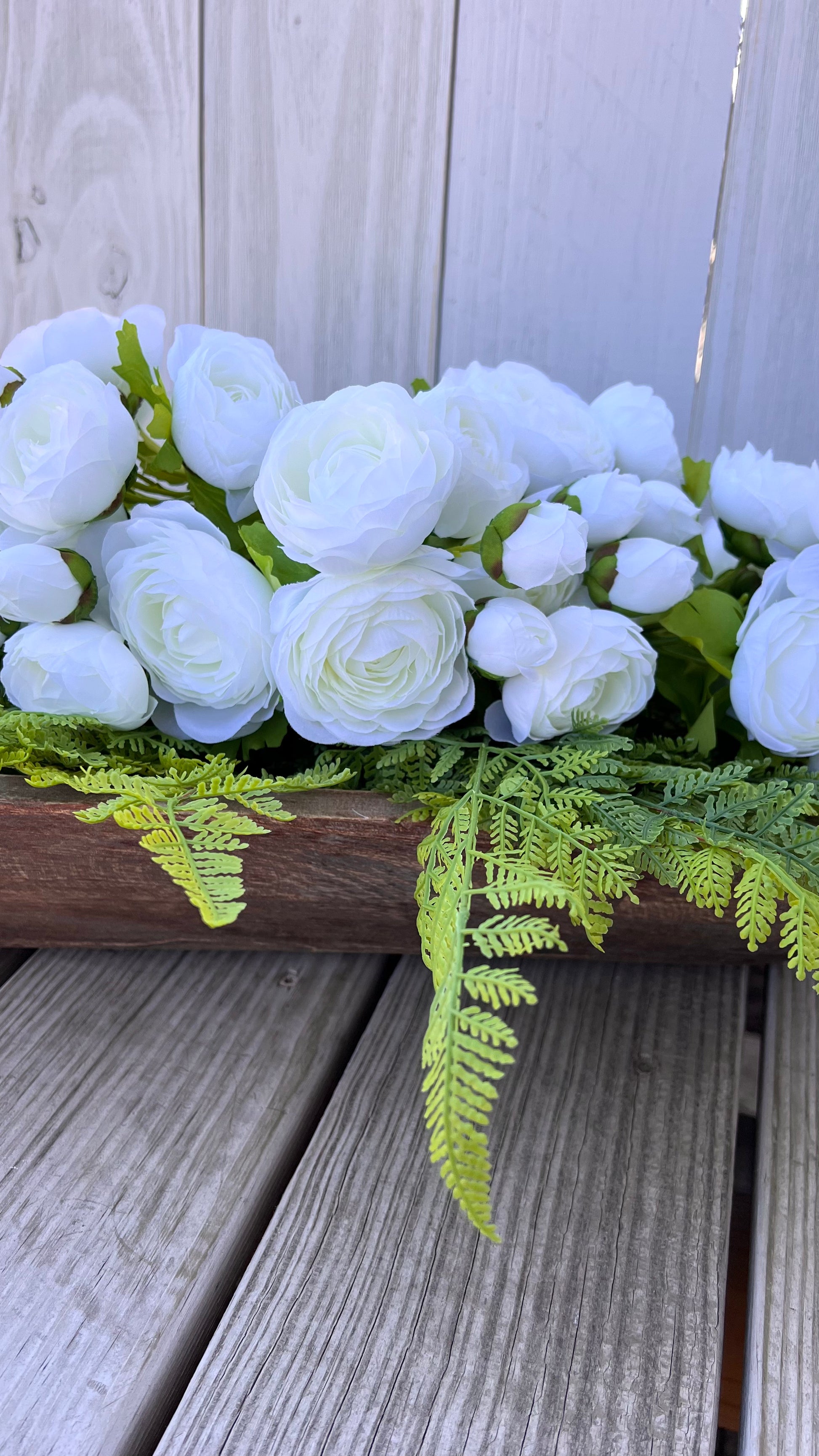 White ranunculus bundle styled in a wooden dough bowl with fern greenery, showing natural movement and depth in a layered composition