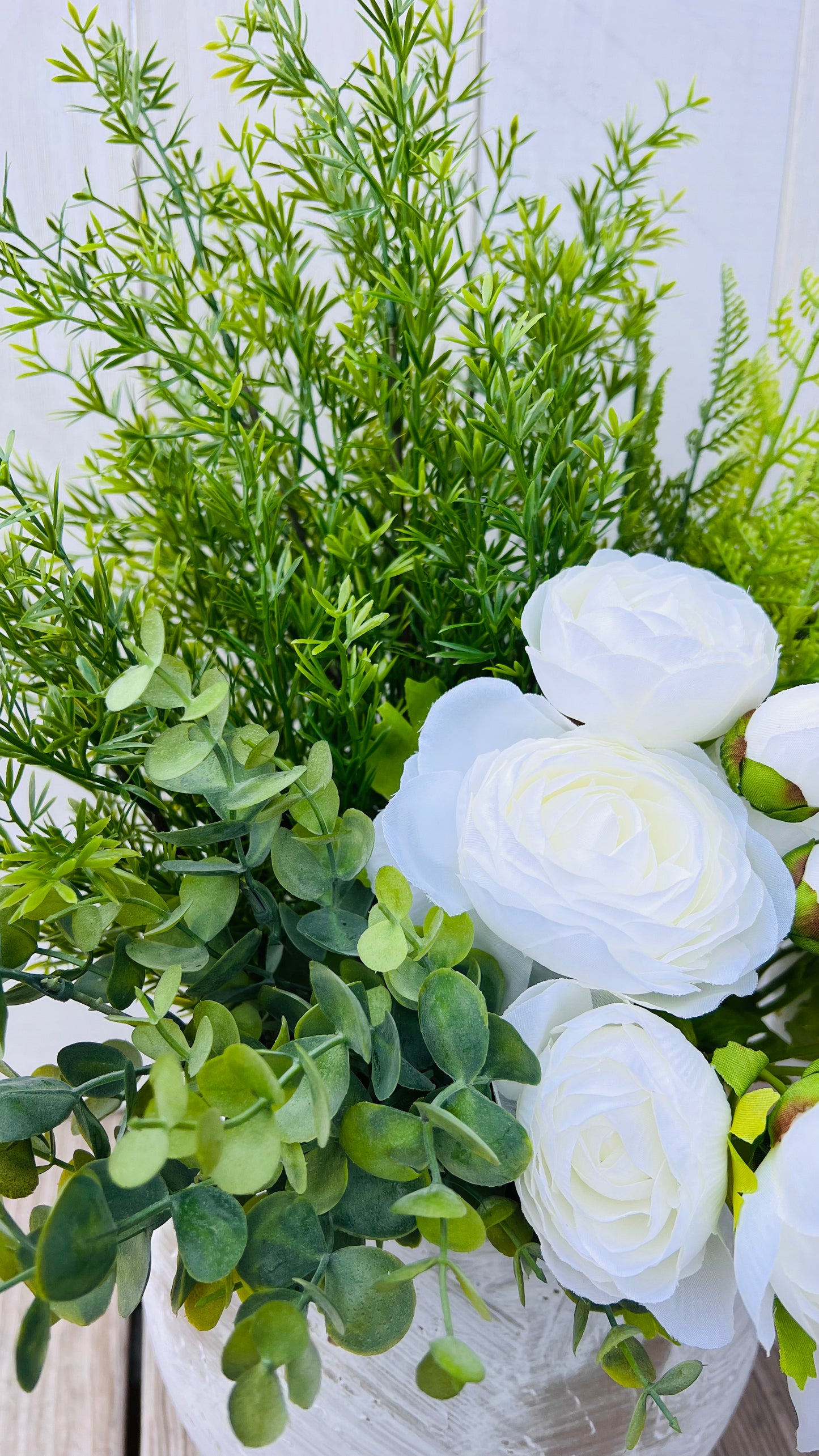 White ranunculus stems styled in a ceramic vase with mixed greenery, showcasing scale and coordination with complementary stems